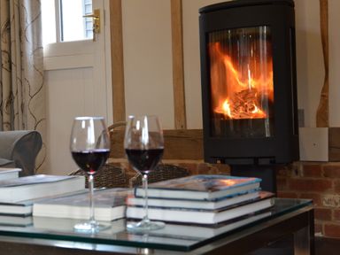A living room with a glass table stacked books two glasses of red wine a fireplace and a door at Bird Cottage Burgh Near Grundisburgh