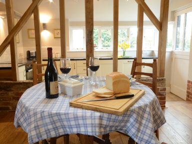 A kitchen dining area with a round table set with bread, wine, and glasses at Bird Cottage Burgh Near Grundisburgh