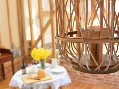 A dining table with bread flowers and wine visible behind a hanging candle lantern at Bird Cottage Burgh Near Grundisburgh