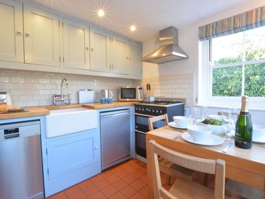 A kitchen with wooden countertop white cabinets dining table set with bowls glasses and a bottle at 1 South Cottages in Thorpeness