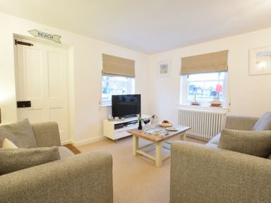 A living room with two sofas a coffee table a television and windows with blinds at 1 South Cottages in Thorpeness