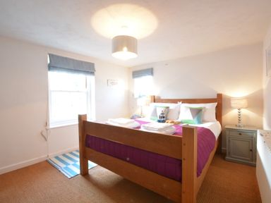 A bedroom with a wooden bed with purple bedding and bedside tables with lamps at 1 South Cottages in Thorpeness