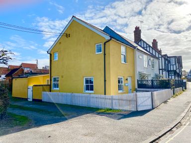 A yellow house with white framed windows and a white picket fence at 1 South Cottages in Thorpeness