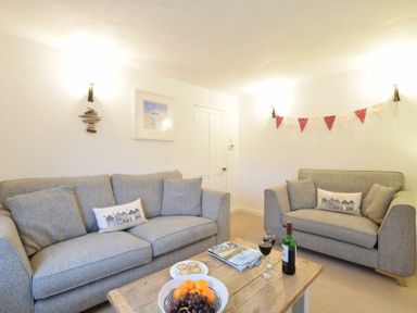 A living room with two grey sofas and a wooden coffee table with fruit and wine at 1 South Cottages in Thorpeness
