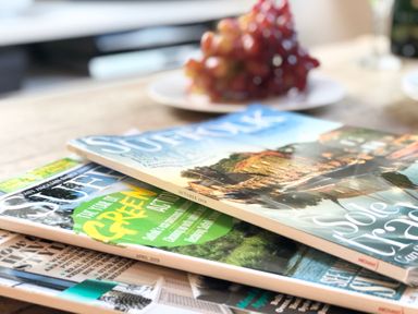 A wooden table with a stack of magazines and a plate of grapes in the background at 1 South Cottages in Thorpeness