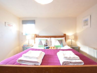 A bedroom with a double bed with purple bedding two folded towels on the bed and bedside tables with lamps at 1 South Cottages in Thorpeness