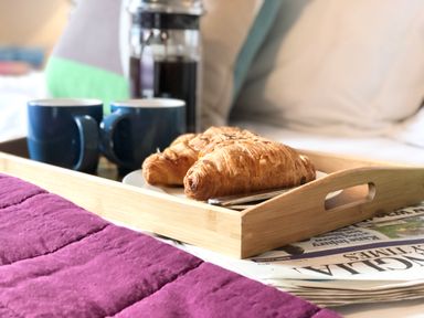 A wooden tray with two croissants on a plate and two blue mugs next to a French press with coffee on a bed at 1 South Cottages in Thorpeness