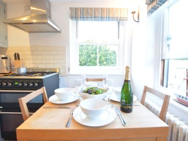 A dining table set with bowls plates glasses and a bottle of champagne in a kitchen at 1 South Cottages in Thorpeness