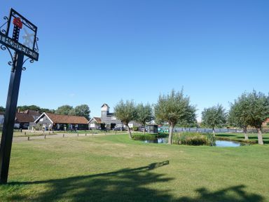 A grassy area with trees a pond and buildings under a clear sky at Thorpeness
