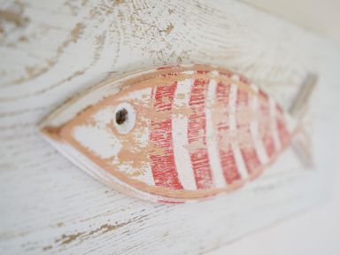 A wooden fish decoration with red and white stripes on a textured white surface at 1 South Cottages in Thorpeness