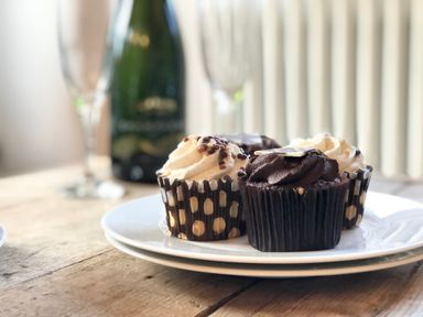 A plate with chocolate and vanilla cupcakes on a wooden table with champagne bottle and glasses in the background at 1 South Cottages Thorpeness