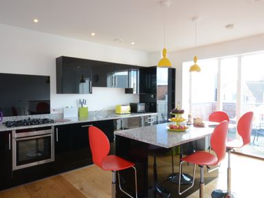 A kitchen with black cabinets yellow pendant lights and red chairs at Parrotfish Bay in Southwold