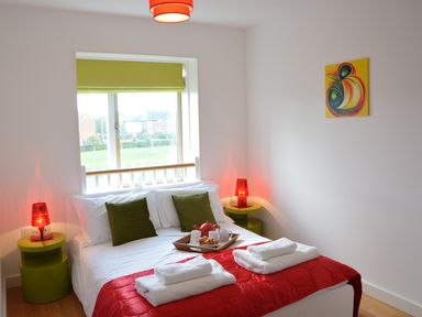 A bedroom with a double bed green pillows red lamps and a window at Parrotfish Bay in Southwold