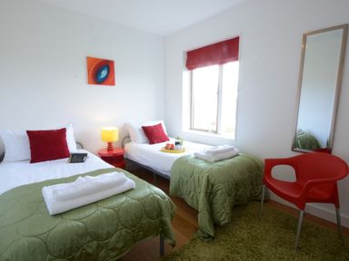 A bedroom with two single beds green bedspreads and red pillows a red chair and a mirror at Parrotfish Bay Southwold