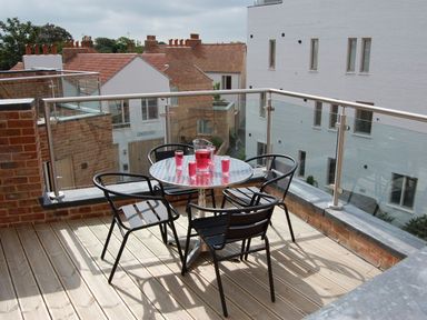 A balcony with a round metal table and four black chairs with a pitcher and four glasses of red drink at Parrotfish Bay in Southwold
