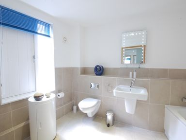 A bathroom with a wall-mounted toilet sink and mirror near a window with blue blinds at Seal Cove in Southwold