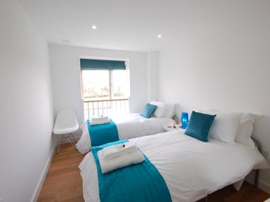 A bedroom with two single beds white chair and a window at Seal Cove in Southwold