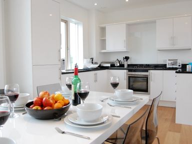 A kitchen with a dining table set with bowls, plates, wine glasses, a bowl of fruit, and a bottle of wine at Seal Cove in Southwold