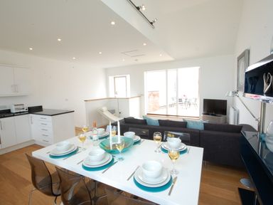 A dining table set for six with plates and glasses in a modern open-plan kitchen and living area at Seal Cove in Southwold
