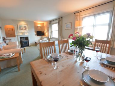 A dining table set with plates glassware and flowers in a living room with sofas a fireplace and a television at Crabbe House in Aldeburgh