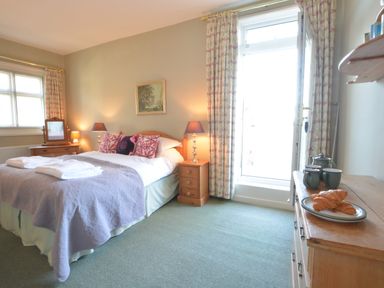 A bedroom with a double bed bedside tables lamps a chest of drawers with cups and croissants and a door with curtains at Crabbe House Aldeburgh