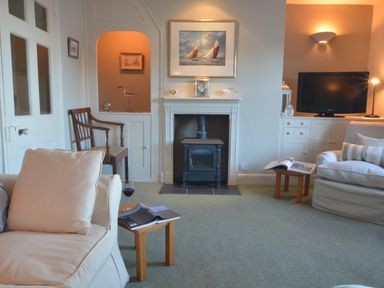 A living room with armchairs a fireplace a television and small wooden tables at Crabbe House in Aldeburgh