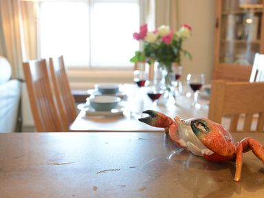 A dining room with a table set with bowls and glasses of red wine and a crab figurine on a counter in the foreground at Crabbe House in Aldeburgh