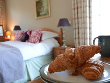 A bedroom with a bed pillows bedside tables lamps and croissants on a plate at Crabbe House in Aldeburgh