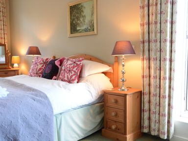 A bedroom with a wooden bed and bedside tables with lamps and floral curtains at Crabbe House in Aldeburgh