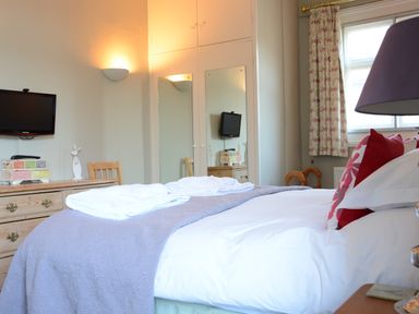 A bedroom with a bed with white and red pillows towels on a grey bedspread a wall-mounted TV and a dresser at Crabbe House in Aldeburgh