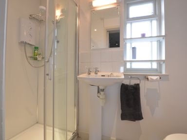 A bathroom with a shower enclosure sink mirror window towel and toilet paper holder at Crabbe House in Aldeburgh