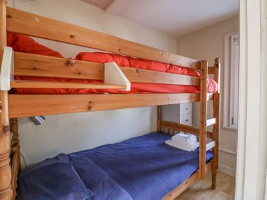 A wooden bunk bed with red bedding on top and blue bedding on bottom with towels on the bottom bed at Crabbe House in Aldeburgh