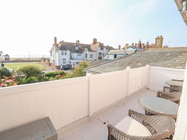 A balcony with wicker chairs and glass tables overlooking houses and the sea at Crabbe House in Aldeburgh