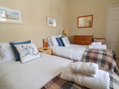 A bedroom with two single beds with pillows and folded towels on plaid blankets a wooden dresser with a mirror and a lamp on a nightstand at Crabbe House in Aldeburgh