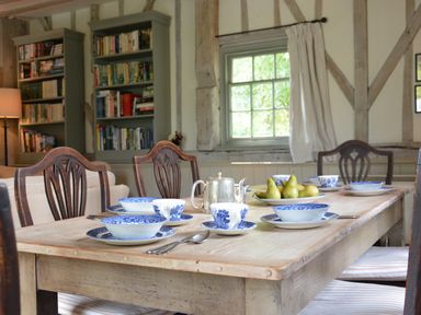 A dining table set with blue and white china teacups and bowls a silver teapot and a plate of pears in a room with wooden beams bookshelves and a window at The Gig House Stowupland