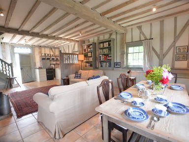 An open living space with a wooden dining table set with blue and white dishes a sofa bookshelves and a kitchen area at The Gig House Stowupland