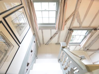 A staircase with framed pictures on the wall and two windows with curtains at The Gig House Stowupland
