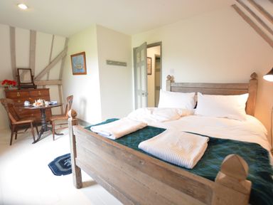 A bedroom with a wooden bed, white bedding, a round table with chairs, a wooden dresser and a doorway at The Gig House, Stowupland