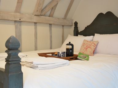 A bed with white bedding pillows a pink floral cushion folded towels and a tray with a coffee press cups and a book at The Gig House Stowupland