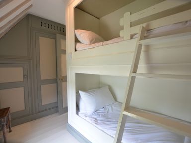 A bedroom with built in bunk beds and a wooden ladder next to a wall with paneled doors at The Gig House in Stowupland