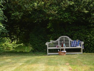 A wooden bench with bottles and a blanket in a garden with trees and bushes at The Gig House Stowupland