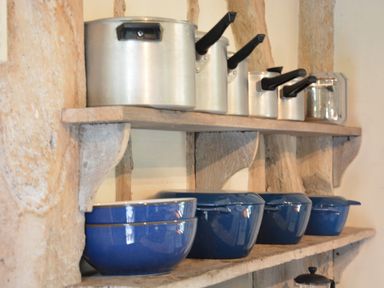 Metal saucepans on a wooden wall shelf above blue ceramic bowls and pots at The Gig House Stowupland