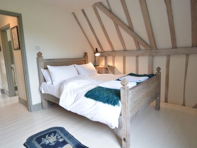 A bedroom with a wooden bed frame white bedding green throw and a small lamp on a wooden shelf at The Gig House Stowupland