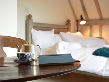 A wooden table with a blue and white teacup and saucer a silver teapot and a closed book in front of a wooden bed with white bedding at The Gig House Stowupland