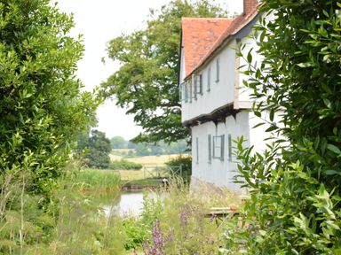 Side view of a white house with open windows next to a garden and pond at The Gig House in Stowupland