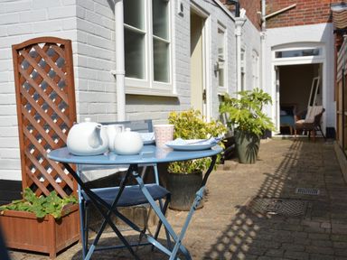 A patio with a blue metal table and chair set with teapots and cups beside a white brick wall with potted plants at Spindrift Southwold