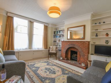 A living room with a brick fireplace bookshelves a television and sofas at Spindrift Southwold