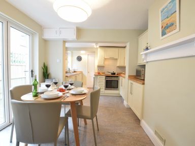 A kitchen and dining area with a round table set with plates and glasses and a bottle of wine at Spindrift Southwold