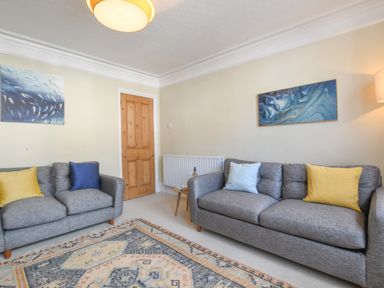 A living room with two gray sofas with colored cushions a wooden door and two blue paintings at Spindrift Southwold