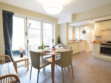 A kitchen and dining area with a round table and four chairs near glass doors at Spindrift Southwold